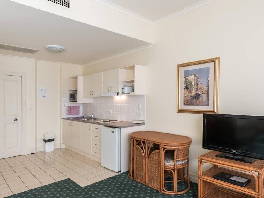 A compact kitchen with white cabinets, a small island, and a flat-screen TV on a stand.