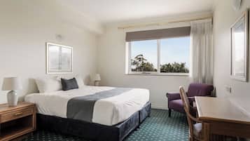 A hotel room with a large bed, a chair, a small table, and a window with a view of trees.