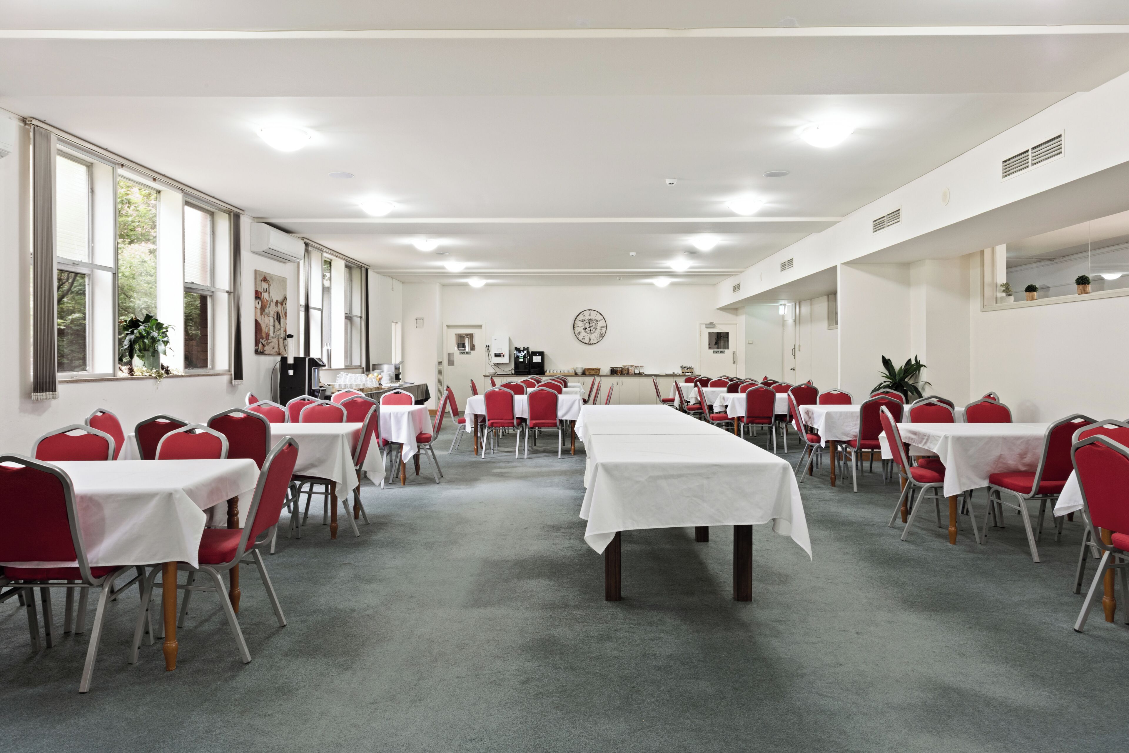 Un salón de conferencias con mesas, sillas, ventanas amplias y un reloj en la pared.