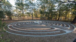 A labyrinth garden with a central circular path surrounded by trees.