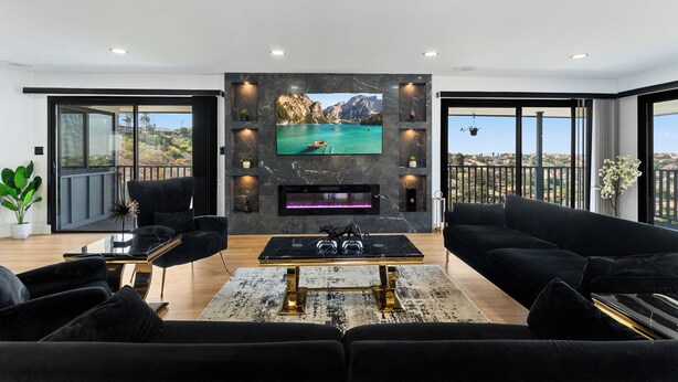 A modern living room with a large TV, black sofas, a marble fireplace, and a balcony with a scenic view. - 3-bedroom house in charming La Mesa with AC (La Mesa)