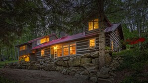 A log cabin with a stone foundation, large windows, and a red roof.