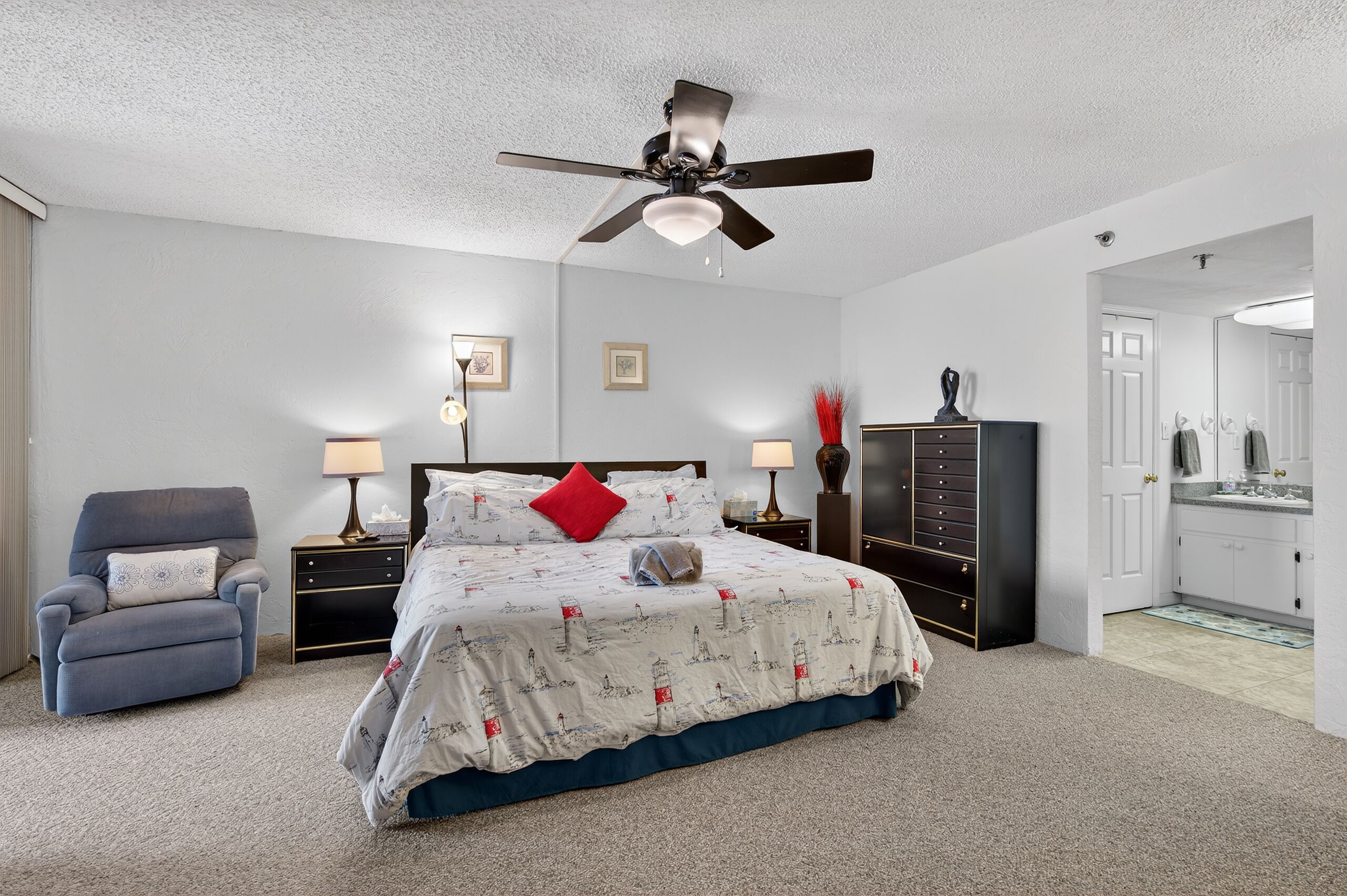Quarto com cama, cadeira, mesa de cabeceira, cômoda e ventilador de teto.