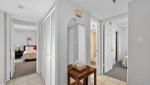 Un pasillo con una mesa de madera, un espejo y una puerta que da a un dormitorio con cama y mesita de noche.