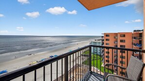 Un balcón con vistas a una playa, un edificio con varios balcones y un cielo despejado.