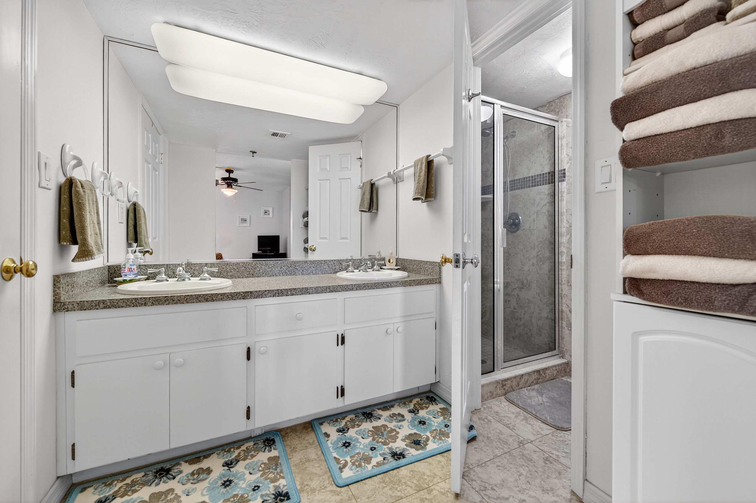 Une salle de bain avec deux lavabos, une douche et un porte-serviettes où sont pliées les serviettes.