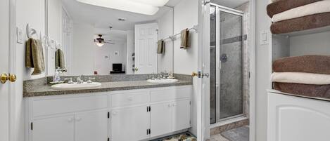 Une salle de bain avec deux lavabos, une douche et un porte-serviettes où sont pliées les serviettes.