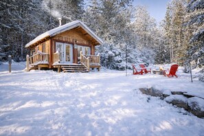 A wooden cabin with a porch, surrounded by snow-covered trees. - Adventure by Day • Hot Tub & Cozy Nights (Bethel)