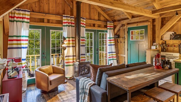 A cozy cabin interior with a wooden ceiling, a dining table, a sofa, and a kitchen area. - Fall Adventures • Private Hot Tub • Sunday River (Bethel)