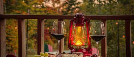 Una mesa de madera con una tabla de quesos, uvas y un farolillo rojo en un balcón con vistas a árboles.