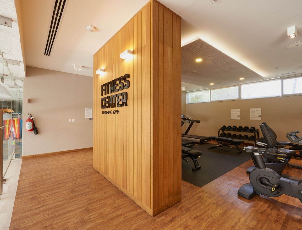 A fitness center with a wooden reception desk, exercise equipment, and a glass wall.