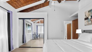 A modern hotel room with a large bed, a wooden ceiling, and a view of the balcony area. - Renovated 3BR w/ AC, Vaulted Ceilings & Lanai Ocean View Near Airport (Kailua-Kona)