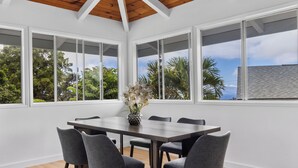 A dining area with a large table and chairs, large windows with a view of trees and a building, and a wooden ceiling. - Renovated 3BR w/ AC, Vaulted Ceilings & Lanai Ocean View Near Airport (Kailua-Kona)