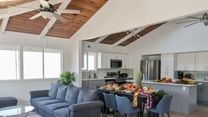 A modern kitchen with white cabinets, a stainless steel refrigerator, and a dining area with a table set for a meal. - Renovated 3BR w/ AC, Vaulted Ceilings & Lanai Ocean View Near Airport (Kailua-Kona)