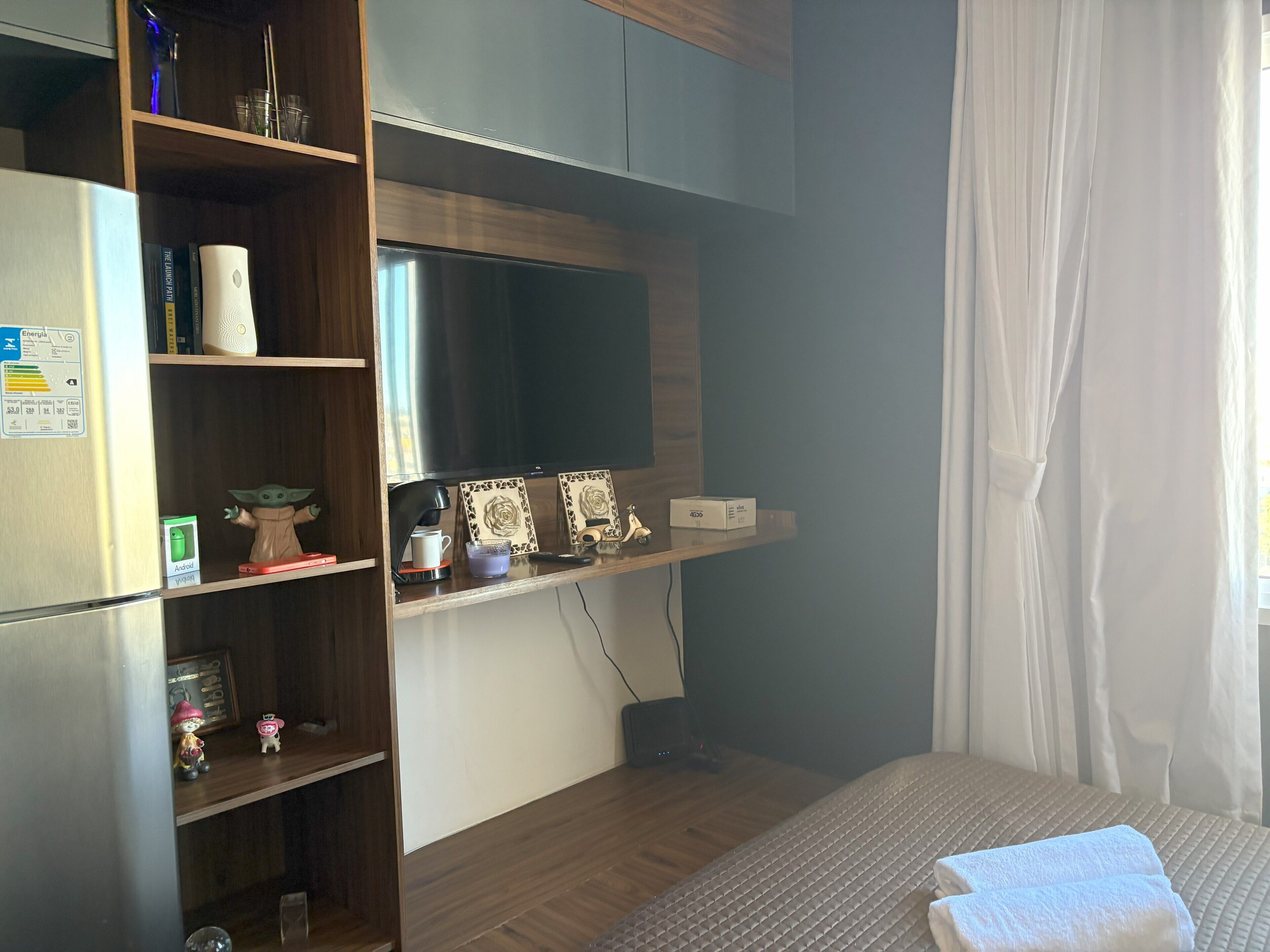 Une chambre d’hôtel avec un lit, un bureau avec un ordinateur, une bibliothèque et une fenêtre avec des rideaux.