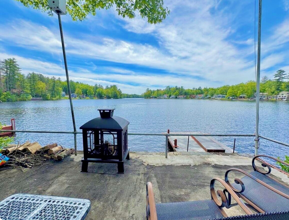 Una terrassa a la vora d'un llac amb una estufa de llenya, una graella metàl·lica i mobiliari exterior.