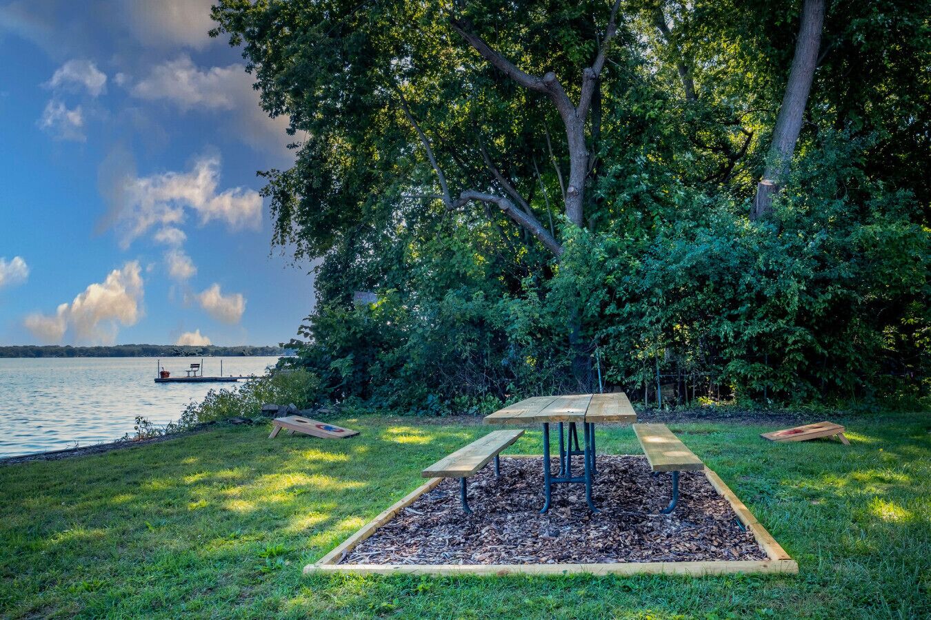 A picnic area with a table and benches, surrounded by trees and a lake.