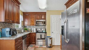 A kitchen with wooden cabinets, a stainless steel refrigerator, a microwave, an oven, and a coffee maker. - Spacious Family Stay, Large Dining, 3 Cozy Bedrooms, Home Near Buckroe Beach (Hampton)