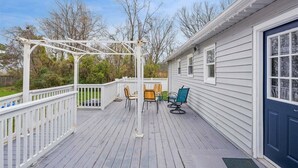 A covered deck with outdoor furniture and a pergola, adjacent to a house with a dark front door. - Spacious Family Stay, Large Dining, 3 Cozy Bedrooms, Home Near Buckroe Beach (Hampton)