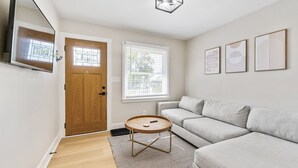 A modern living room with a light-colored sofa, a round coffee table, and a wooden door. - Fox Island Lakefront Retreat (Lakeview)