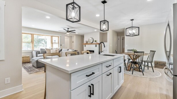 A modern kitchen with a central island, pendant lighting, and a dining area with a wooden table and chairs. - Fox Island Lakefront Retreat (Lakeview)