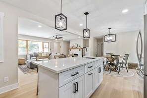 A modern kitchen with a central island, pendant lighting, and a dining area with a wooden table and chairs. - Fox Island Lakefront Retreat (Lakeview)