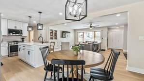 A modern kitchen with white cabinets, a central island, and a dining area with a round table and chairs. - Fox Island Lakefront Retreat (Lakeview)