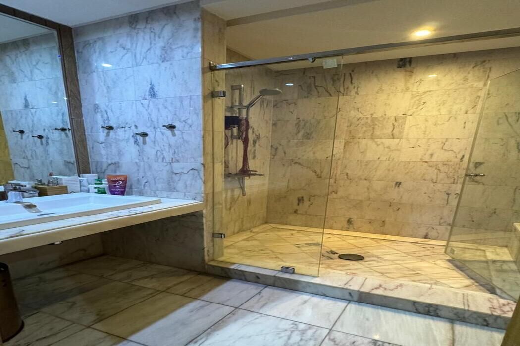 Een badkamer met een douche met glazen wand, marmeren wanden en een wastafel met toiletartikelen.