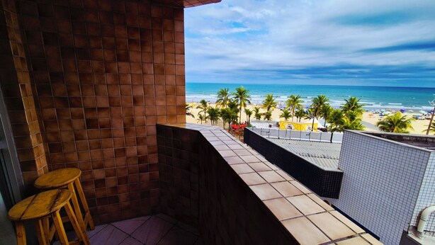 A balcony with a view of a beach, palm trees, and a clear sky. - Neri House - Ocean View, Beach Front (Cidade Ocian Praia Grande)