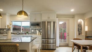 Una cocina moderna con armarios blancos, electrodomésticos de acero inoxidable, una isla grande y un comedor con sillas de madera.