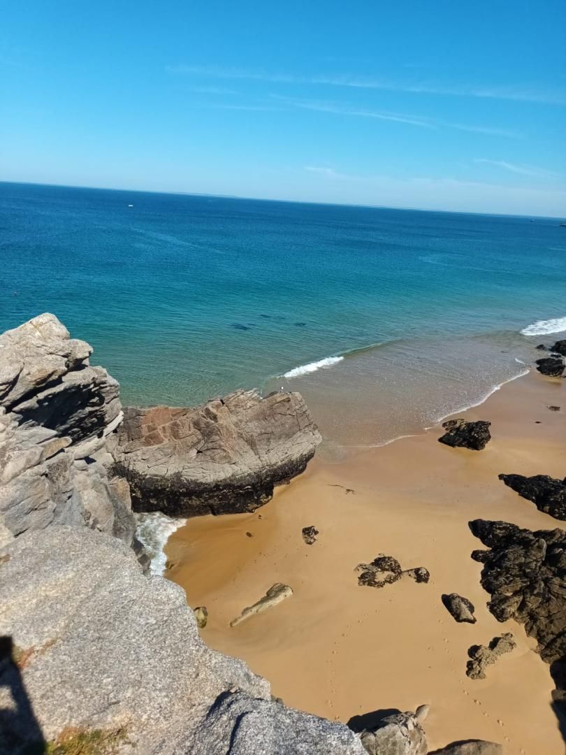 A coastal beach with clear blue water, sandy shore, and large rocks.
