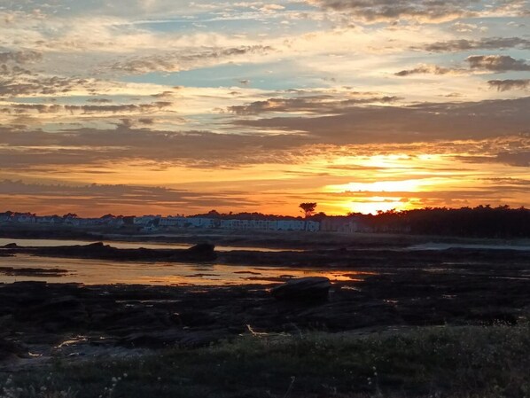 A sunset over a coastal landscape with buildings in the distance.