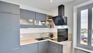 A modern kitchen with grey cabinets, a wooden countertop, a built-in oven, and a window with a view of the street.
