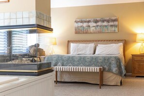 A bedroom with a bed, a bench, a fireplace, a painting, and a lamp. - Coast to Coast:Dog Friendly, Private Pool, Hot Tub, Community Amenities (Corolla)