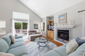 A spacious living room with a fireplace, a television, and a balcony. - Coast to Coast:Dog Friendly, Private Pool, Hot Tub, Community Amenities (Corolla)
