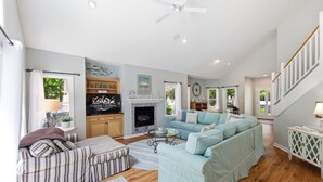 A spacious living room with a fireplace, a large sofa, a television, and a staircase. - Coast to Coast:Dog Friendly, Private Pool, Hot Tub, Community Amenities (Corolla)