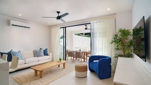 A modern living room with a sofa, coffee table, and blue armchair. There is a dining area with a table and chairs, and a large plant. - NEW villa with plunge pool, 3 mins to beach - Sorrento 10 (Lower Carlton)