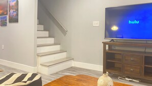 A living room with a large flat-screen TV displaying 'hulu', a staircase, and a wooden coffee table. - Chic Spacious Downtown Home - 5 Mins To Frederick Health Hospital & Fort Detrick (Frederick)