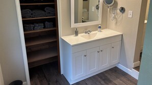Une salle de bain avec un meuble-lavabo blanc, un miroir, un porte-serviettes et une étagère où sont pliés des serviettes.