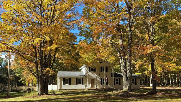 Une maison à deux étages avec un porche à l’avant, entourée d’arbres aux feuilles d’automne.
