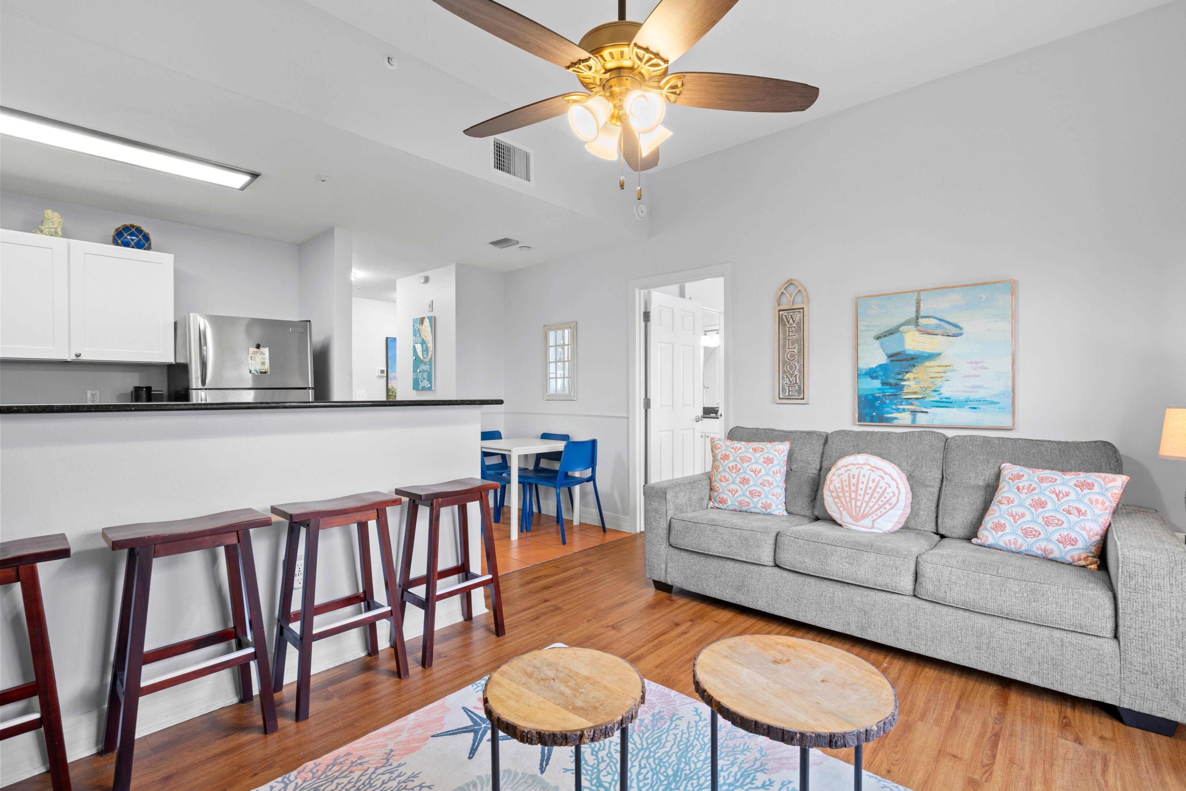 A modern kitchen with a built-in refrigerator, a dining area with bar stools, and a living room with a gray sofa and decorative pillows.