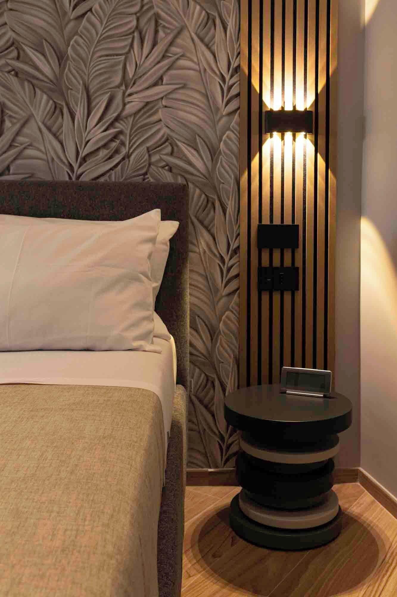 A modern bedroom with a patterned headboard, a bedside table with a flat-screen TV, and a wall-mounted light fixture.
