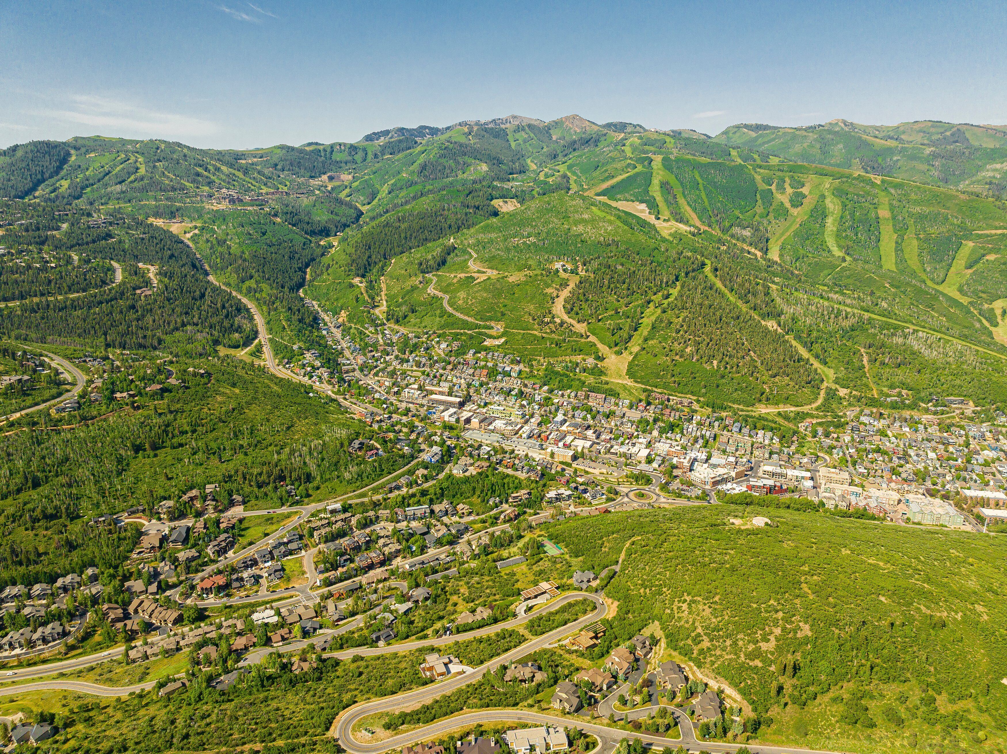 An aerial view of a town nestled in a valley with winding roads and surrounded by forested hills.