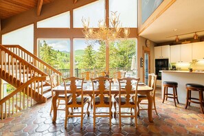 A dining area with a stone floor, wooden chairs, a chandelier, and a view of the outdoors.