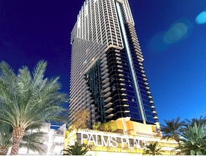 Un edificio alto y moderno con un llamativo letrero que dice 'PALMS PLACE' en la base.