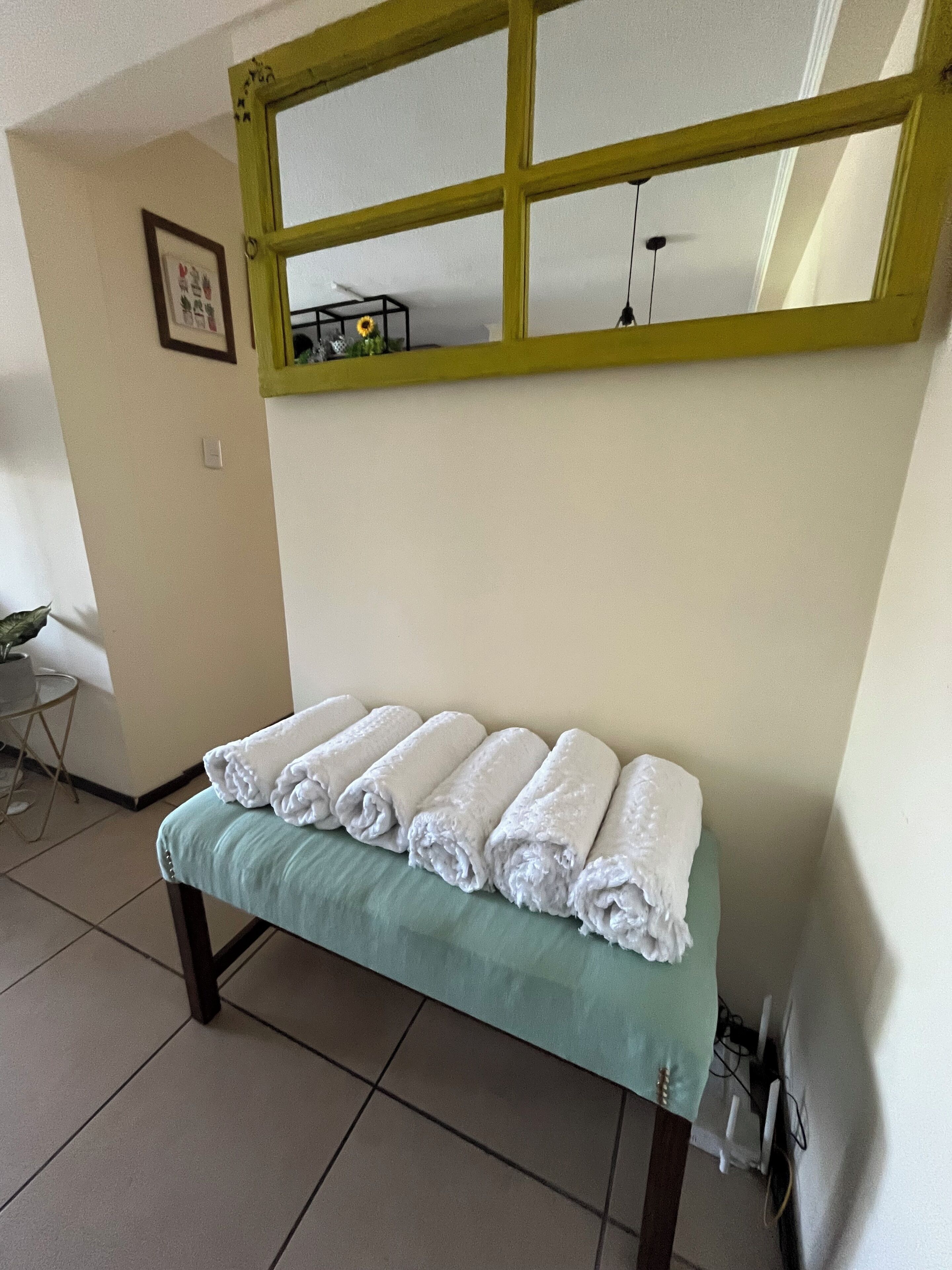 Habitación con un banco cubierto de toallas blancas impecables, un banco verde y un espejo con marco amarillo.