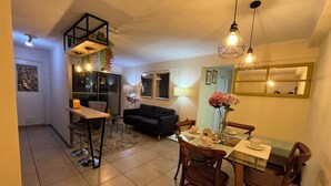 A modern living room with a sofa, dining table, and chairs. There is a kitchen area with a refrigerator and a window. - 10 minutes from International Airport, Vespucio business sector. (Renca)