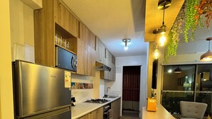 A modern kitchen with a stainless steel refrigerator, wooden cabinets, a gas stove, and a dining area with a table and chairs. - 10 minutes from International Airport, Vespucio business sector. (Renca)