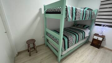 A bunk bed with a patterned bedspread, a small wooden stool, and a nightstand with a decorative item.