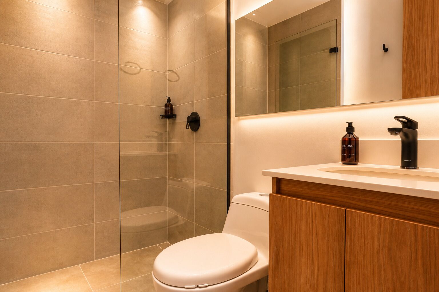 A modern bathroom with a glass-enclosed shower, a toilet, and a vanity with a mirror and two bottles.